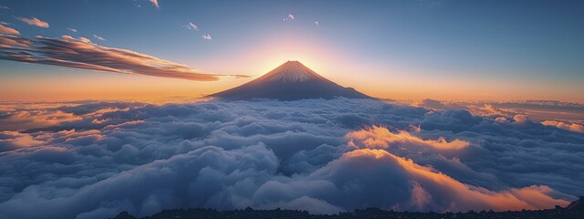 The isolated mountain peak stands majestically above a blanket of clouds as the sun begins to rise. - obrazy, fototapety, plakaty