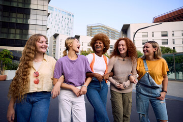 Multiracial group of only smiling young women friends walking hugging on street city center. Happy tourists on girls meeting strolling embracing outdoors. Generation z tourism people enjoying together
