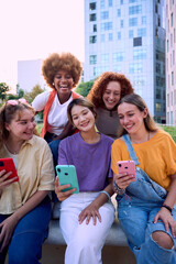 Vertical. Multiracial happy smiling girl friends using phone and smiling together outdoor. Only women group addicted to technology and social media. Fun young and networks as means of communication.