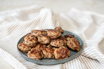 A rustic presentation of golden meatballs arrayed on a ceramic plate, against the soft lines of a crumpled striped napkin, ideal for a cozy dinner setting.
