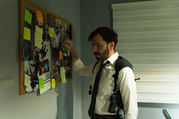 Investigator intensely reviews a board covered with photos and connected clues