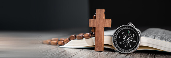 Open Bible on wooden table, compass on it and wooden cross, word of God as guidance concept