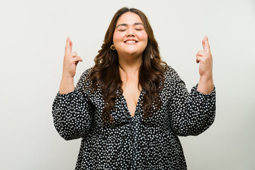 Radiant plus-size lady with closed eyes crossing her fingers, expressing hope and optimism - 790415908