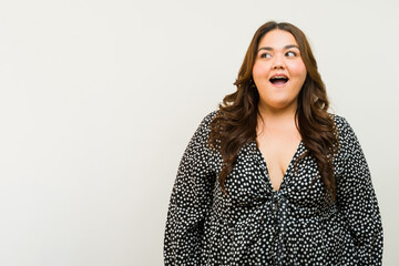 Happy plus-size woman beaming and looking to one side towards copy space in a studio - 790416123