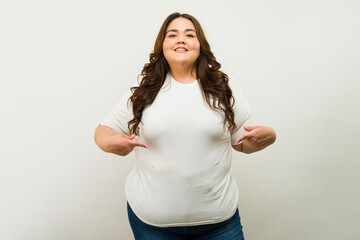 Smiling plus-size woman standing proudly in a white tee and jeans against a neutral backdrop - 790416168