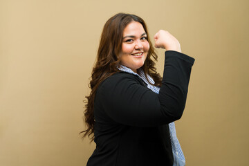 Confident plus-size businesswoman shows off her strength with a smile, posing against a neutral background - 790416758
