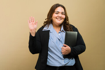 Beautiful fat Hispanic businesswoman with a laptop, gesturing a greeting in a studio - 790416928