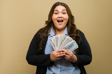 Joyful plus-size woman holding a fan of cash in the studio