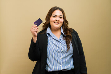 Cute plus-size businesswoman proudly displaying a credit card in a studio setting - 790417393