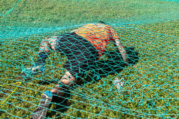 an athlete crawling under a net at an obstacle course race, ocr race