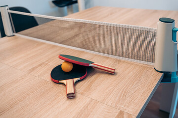 Pingpong paddles and net on indoor table at home. Portable mini pingpong set installed on a wooden...