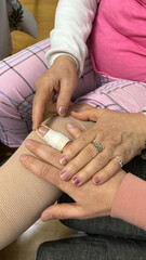 Hand of young anonymous man with injured finger on injured knee of grandmother. Loving family care at home.