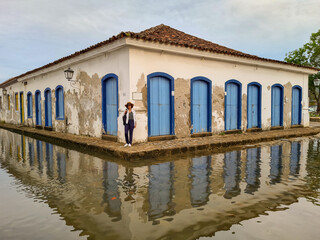 Woman on the sidewalk of an old colonial-style house reflected in the water at high tide