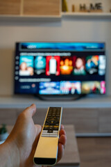 Hand of unrecognizable person holding remote control with television in front. Preparing to change channels. Thinking of choosing and preparing a series on online movie platform.