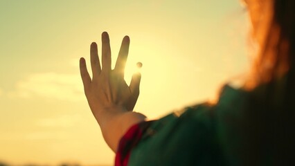 Happy teenage girl touches sun with her fingers. Child holds out his hand at sunset. Hand of happy...