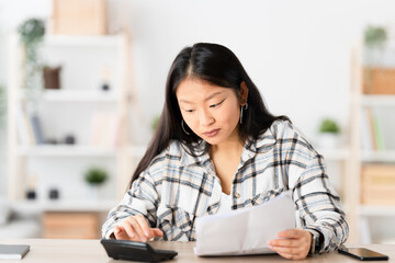 Chinese woman managing home finances using calculator sitting in the living room