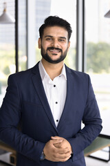 Positive confident company director in formal jacket posing for corporate business portrait, looking at camera with confidence hand gesture, smiling. Professional vertical shot