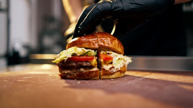 close-up of the hands of a chef in an establishment cutting a ready-made burger lying on board with a knife