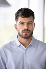 Serious young Arab business man in formal shirt looking at camera, standing for vertical portrait. Attractive male professional, CEO, company owner, entrepreneur head shot