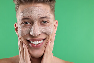 Handsome man applying facial mask onto his face on green background. Space for text