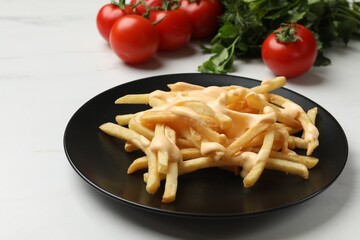 Delicious French fries with cheese sauce, tomatoes and parsley on white table, closeup