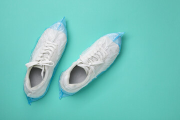 Sneakers in shoe covers on turquoise background, top view. Space for text
