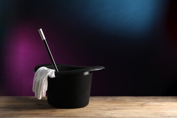 Magician's hat, gloves and wand on wooden table against dark background, space for text