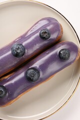 Delicious eclairs decorated with blueberries on white background, top view