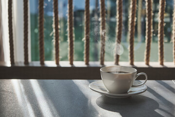a morning hot coffee in white cup in sunshine scene with shade and white smoke from hot water