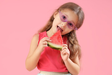Happy little girl in sunglasses eating fresh watermelon on pink background