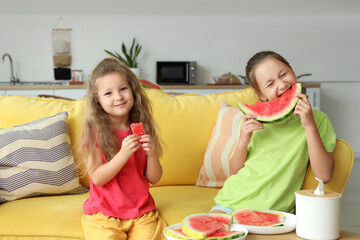Happy little girls with fresh watermelon sitting on sofa in living room