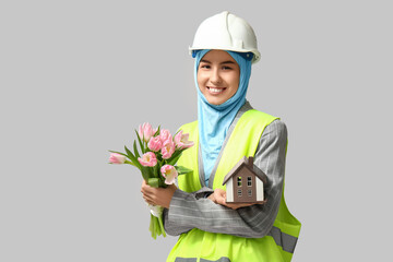 Muslim female construction worker with toy house and pink tulips on white background. Women's Day celebration