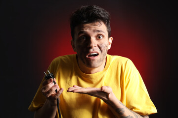 Electrocuted young man with burnt face and plug on dark background, closeup