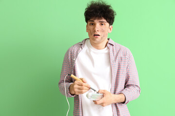 Electrocuted young man with burnt face repairing lamp on green background