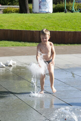 A boy playing with water in park fountain. Hot summer.