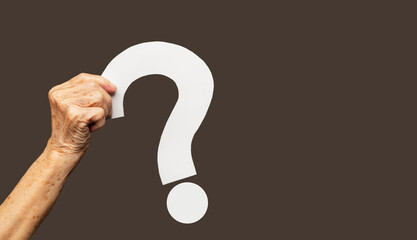 Hand holding a white question mark symbol against a brown background.