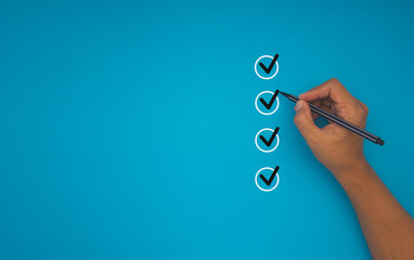 Close-up of hand holding a pen, mark four correct sign symbols in boxes on a blue background.