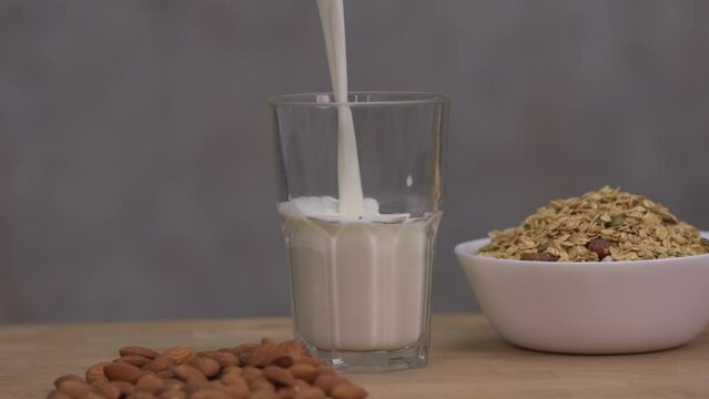 Pour milk into the glass placed on the table. Contains almond seeds Place on the wooden table surface and the granola seeds and grains in the bowl.
