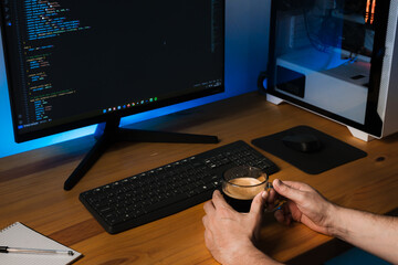 Programmer drinking coffee at desk with blue light