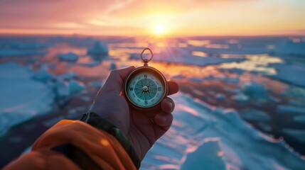 A hand holding a compass in front of a frozen sea at sunset.