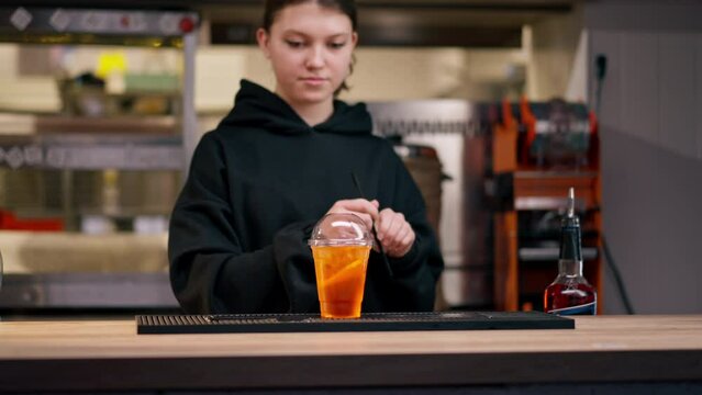 in a professional kitchen behind the bar girl covers a drink with a lid and inserts a straw