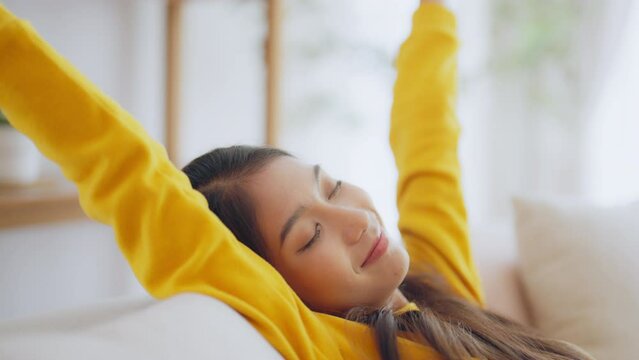 Relaxed young Asian woman enjoying rest on comfortable sofa, calm attractive girl relaxing on couch, breathing fresh air with eyes closed, meditating at home