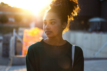 Back lit young pensive African American woman outdoors during sunset.