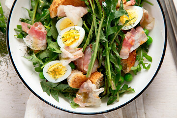 Summer fresh salad from dandelion leaves, eggs, bacon and with bread on light background