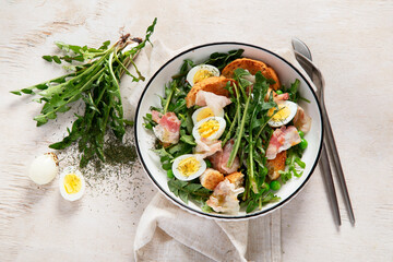 Summer fresh salad from dandelion leaves, eggs, bacon and with bread on light background
