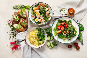 Spring fresh food with green leaf. Salads with strawberries, bacon and ravioli on light wooden background
