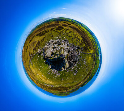 Aerial 360 tiny planet view of peak of rocky mountain with hiker standing on top.