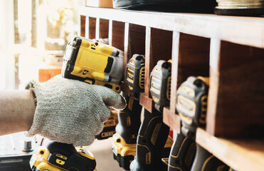 Mechanic reaching for electric screwdriver or electric drill or impact tool on Cordless Tool Shelf Holds  to repair motorcycle in garage. maintenance and repair concept . selective focus