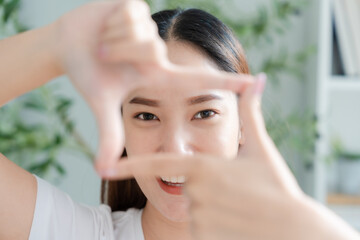 Young asian woman happy and making frame with fingers at living room