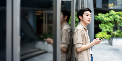 Portrait of handsome Asian student using smartphone. A young man standing outdoor happy smiling...